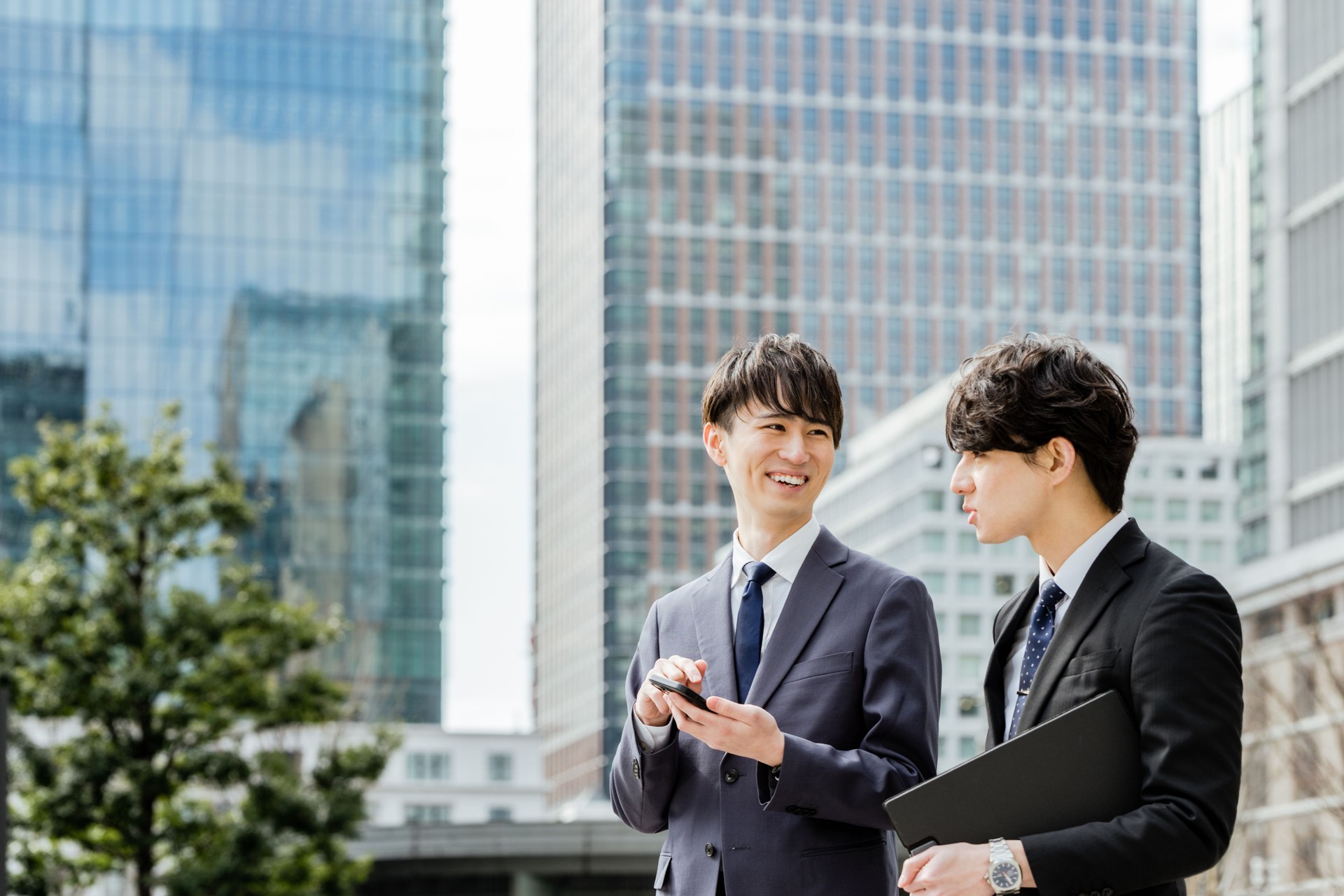 Two men in a suitable suit in their 20s and 30s who have fun talking outdoors in urban areas surrounded by skyscrapers